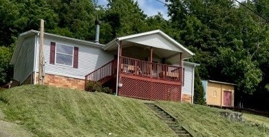 image of manufactured home on a hill. the house has a wooden porch on the front.