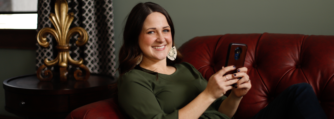 young woman reclining on sofa and using mobile phone